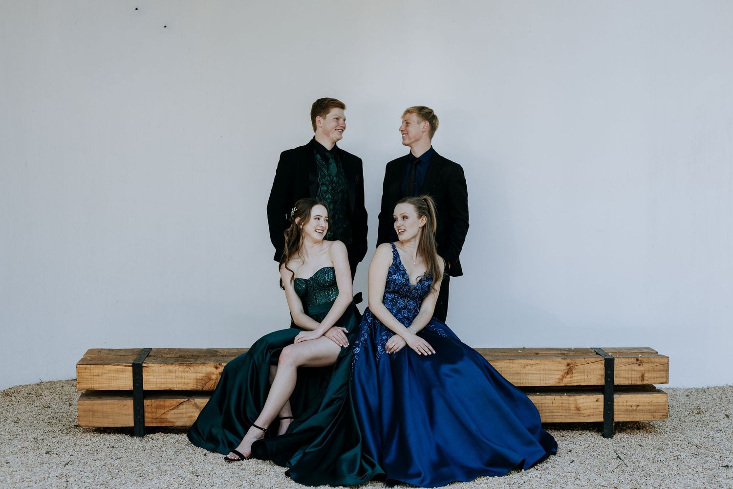 Couple in formal attire sits together on wooden bench in artistic photo series against white wall.