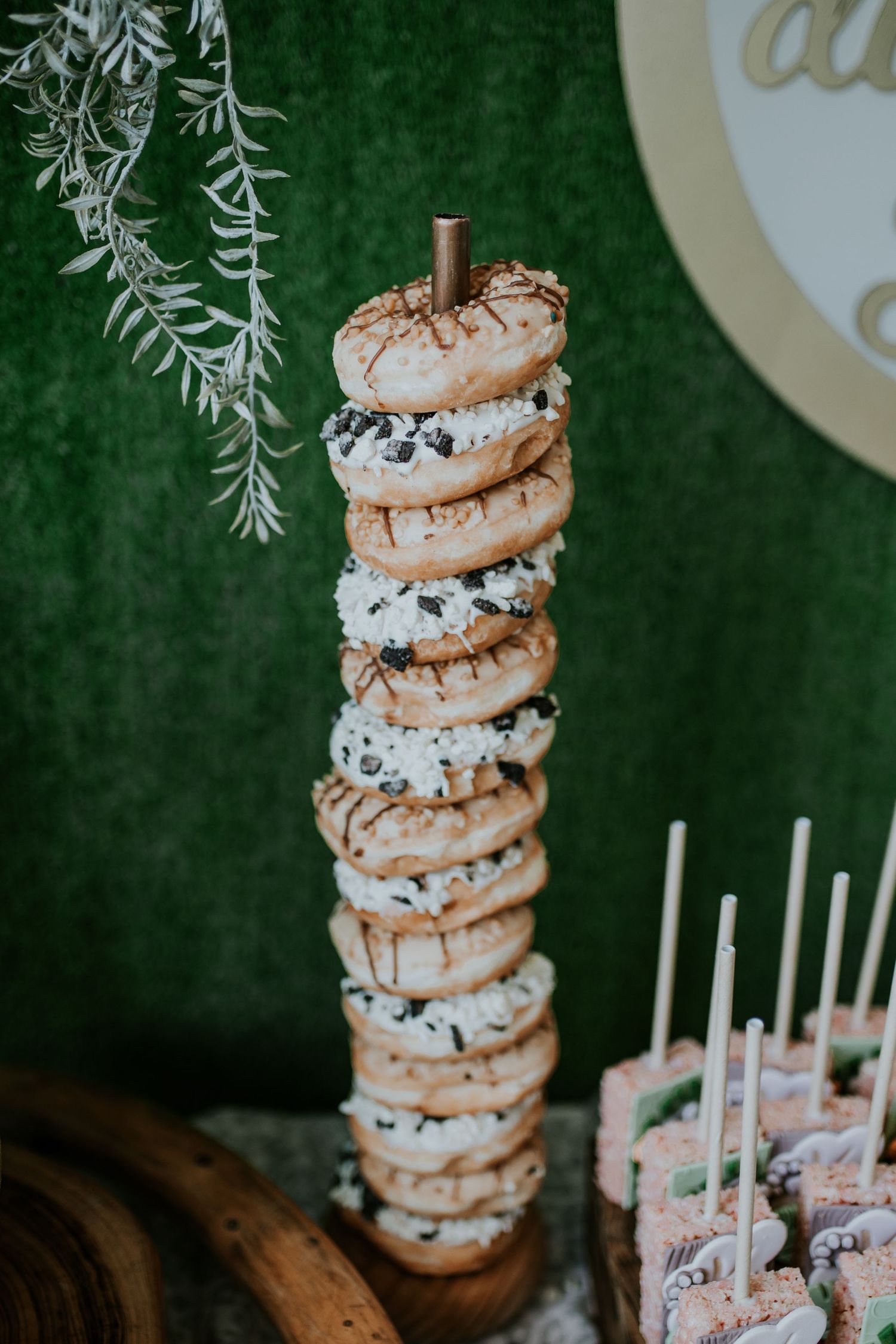 Stacked macarons with chocolate and cream fillings displayed on a vertical holder against a green backdrop.
