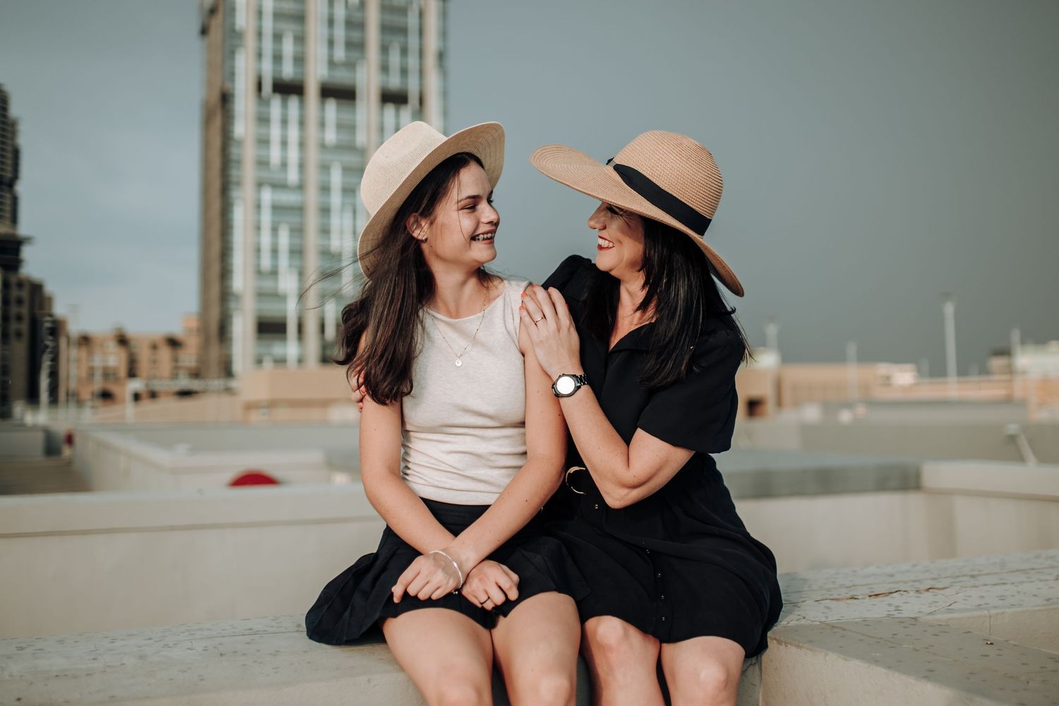 Two people sit and laugh together at the beach on a sunny day.