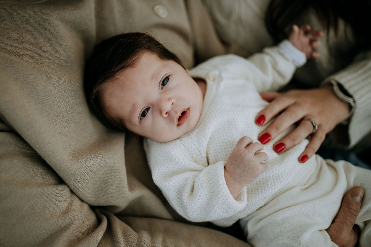 Sweet baby in white sweater rests peacefully on couch with natural window lighting.