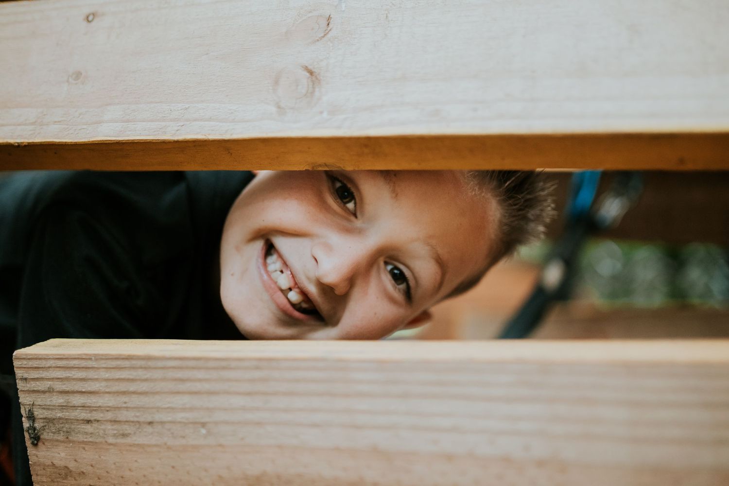 A person playfully peeks through wooden slats while making eye contact with the camera.