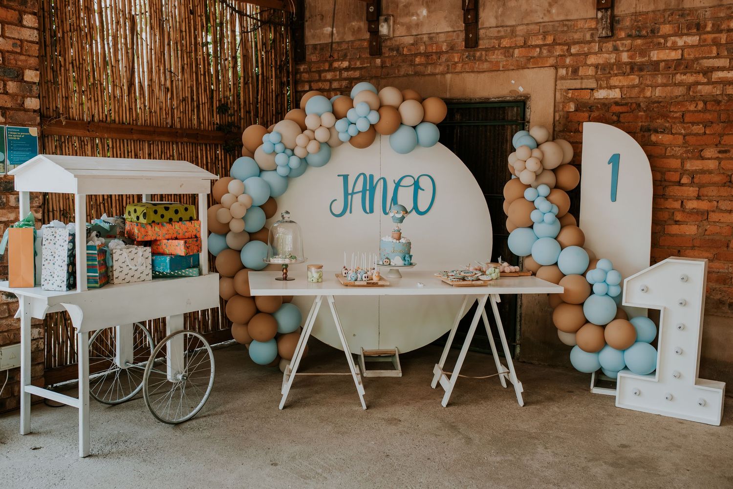 A baby shower party setup with rustic brick walls and blue balloon decorations in an industrial-style venue space.
