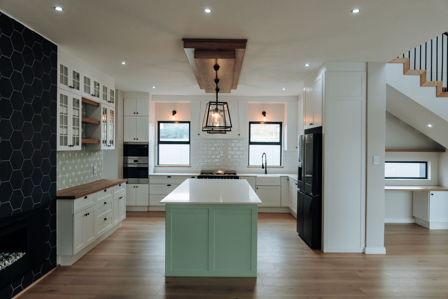 Modern white kitchen with recessed lighting, mint green cabinets, and black accent wall leading down a bright hallway.