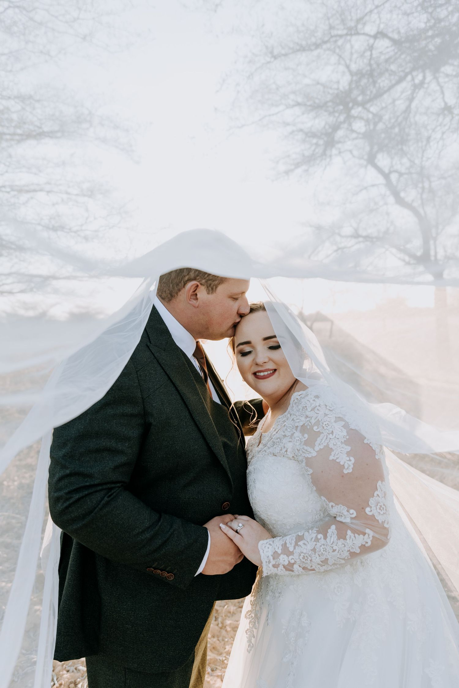 A couple sharing tender moments in wedding attire on a misty day against a soft ethereal background.