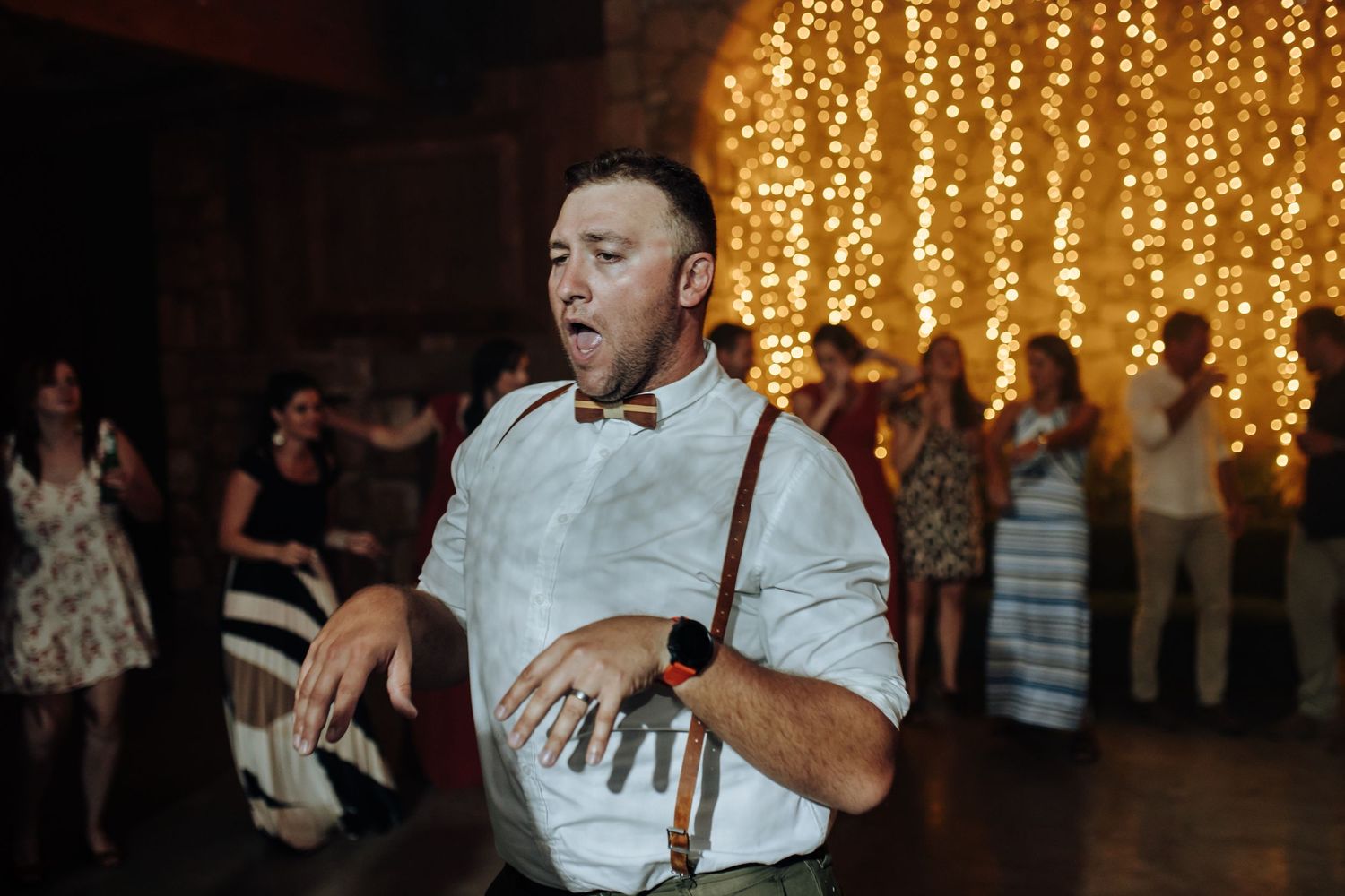 People dancing at a wedding celebration with warm glowing string lights decorating the ceiling.