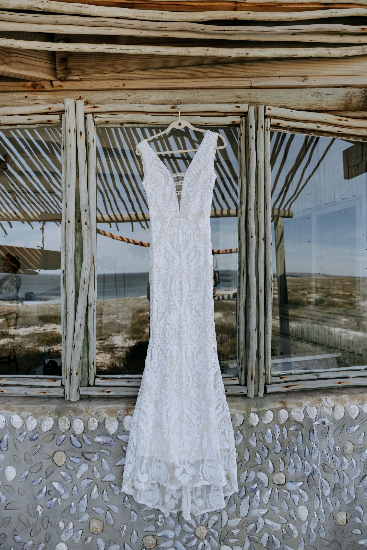 A row of similar white lace wedding dresses hanging on display in a rustic wooden venue with large windows.