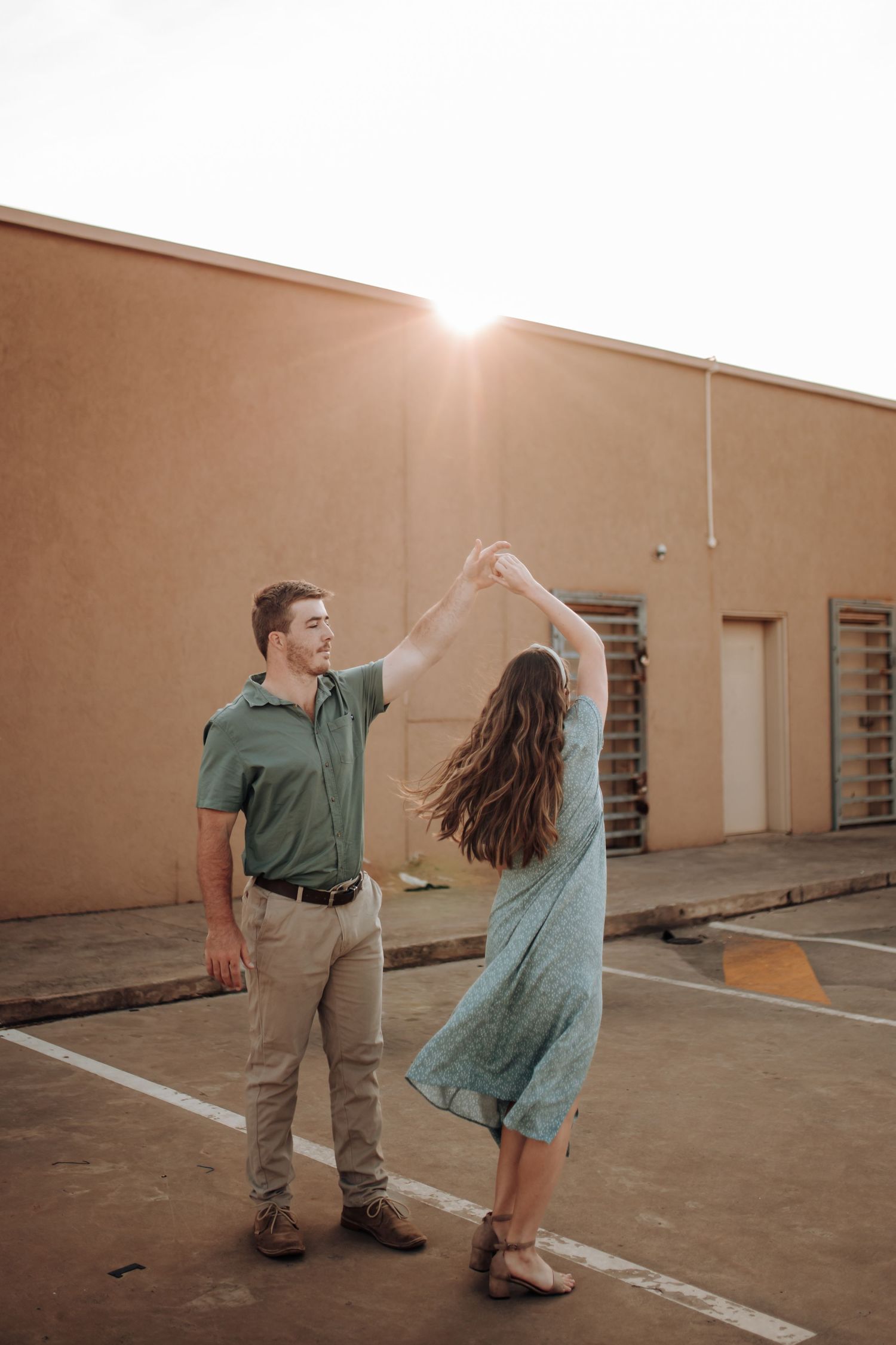 Two dancers move gracefully in a warm sunlit urban space against a terracotta wall.