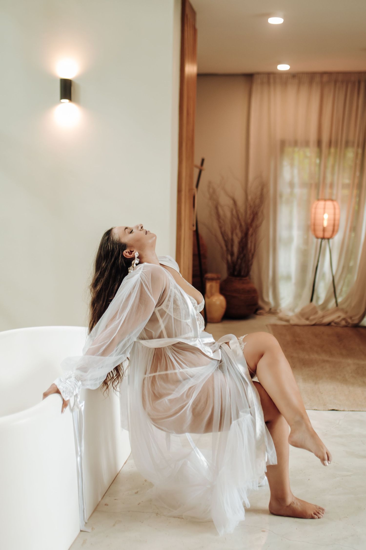 A figure in white sheer fabric reclines gracefully across a bright minimalist interior space.