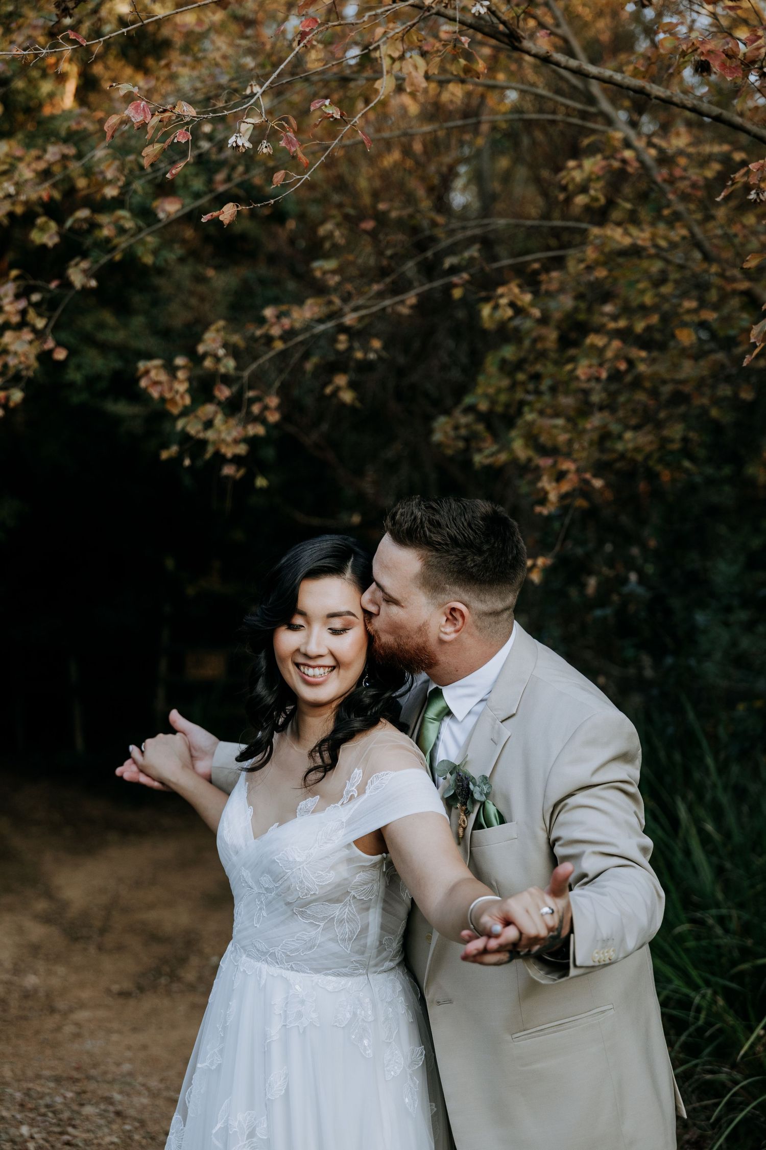 A joyful couple in wedding attire share a lighthearted moment against autumn foliage.