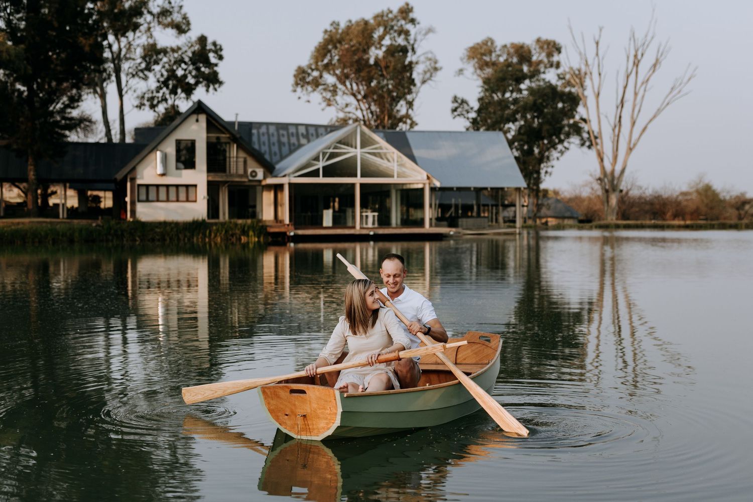 A couple shares a romantic moment while standing on a wooden dock at sunset by a tranquil lake with reflections.