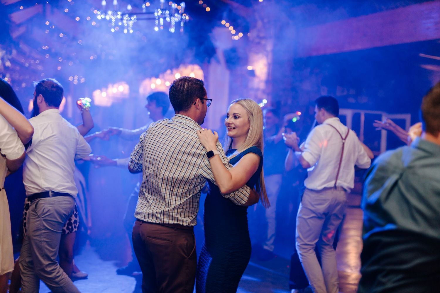 People dancing and socializing at a lively party venue illuminated by blue lighting and atmospheric effects.