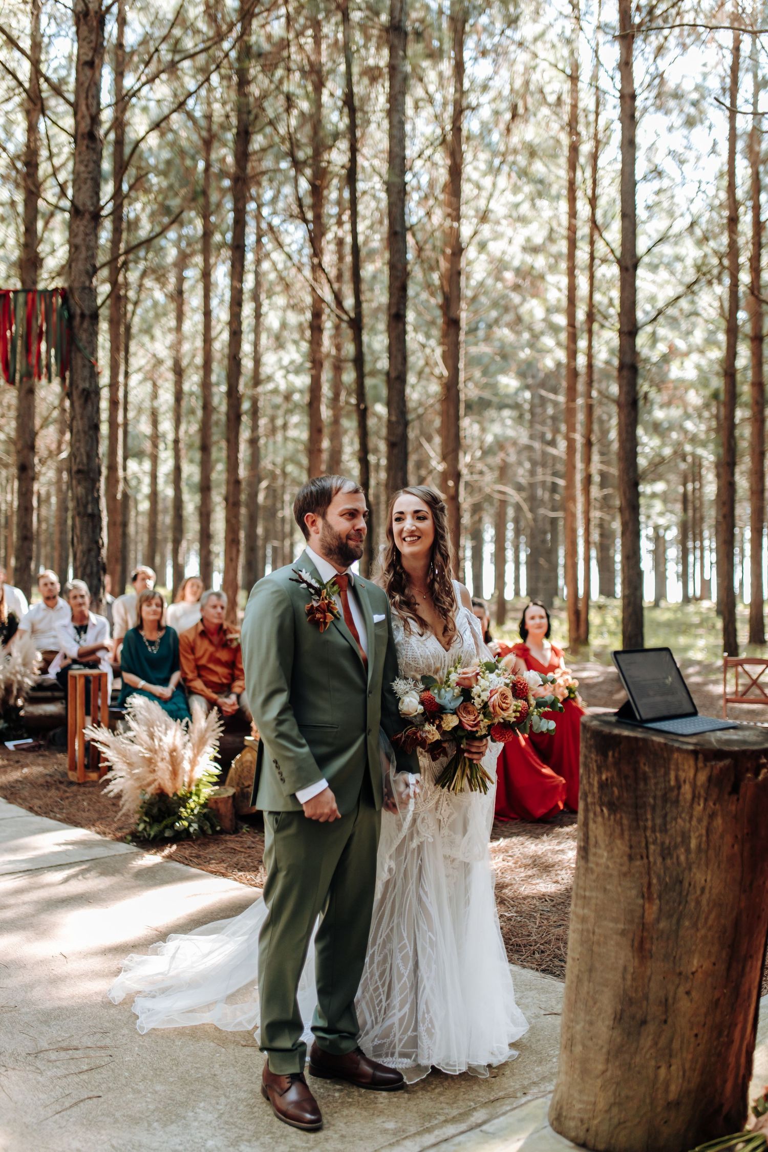 A romantic outdoor wedding ceremony in a pine forest setting with rustic wooden decorations and pink floral accents.
