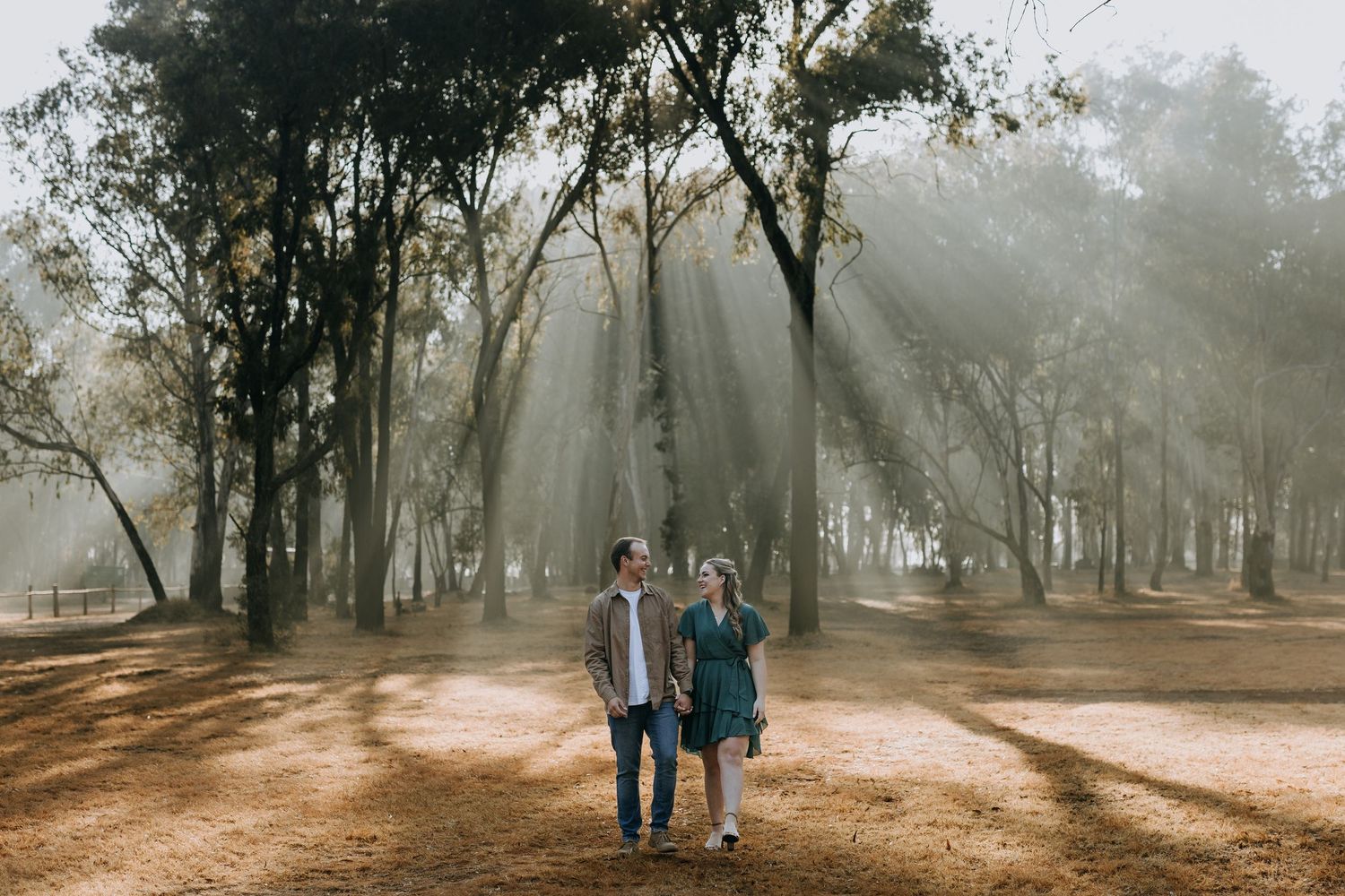 Two people walk together on a misty forest path surrounded by tall trees and soft morning light.
