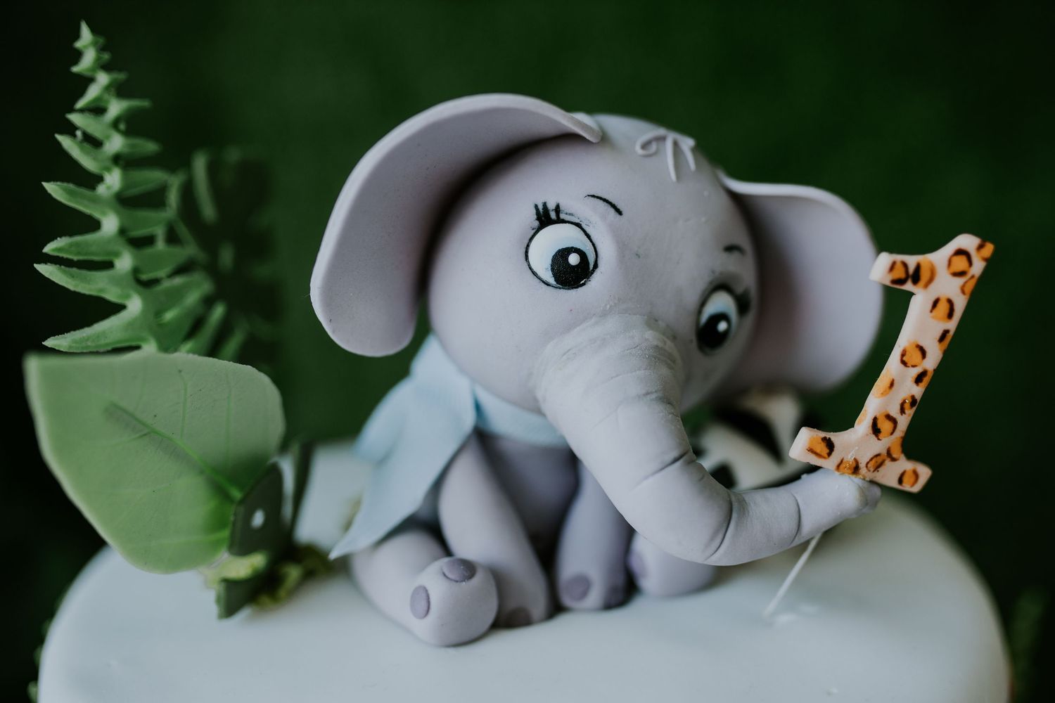 A small plush elephant toy sitting among green leaves and branches in a natural outdoor setting.