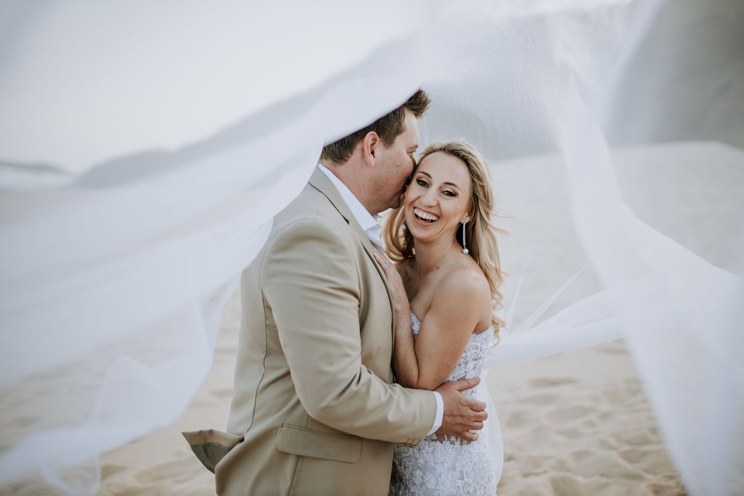 Romantic beach wedding photoshoot showing couple embracing on sandy shore with flowing white dress.