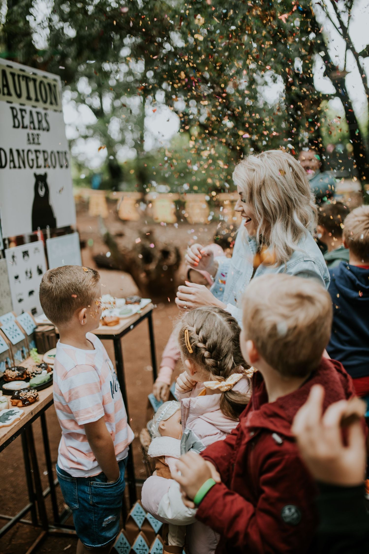 Children enjoying confetti being thrown at an outdoor party while standing near warning signs.