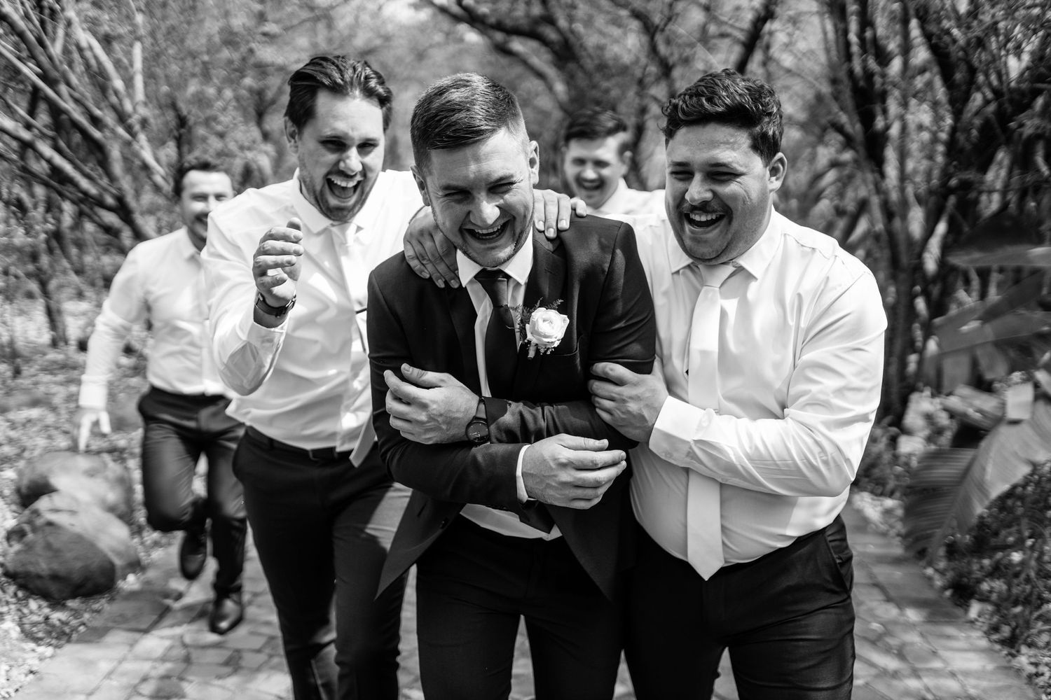 Wedding party members in black and white attire share laughter while looking at something on their phones.