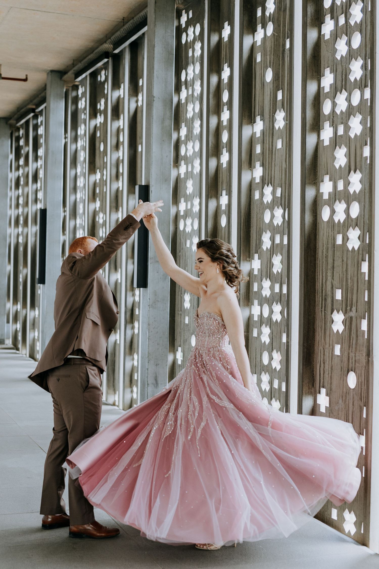 A couple dances in a hallway with glowing string lights, the bride wearing a flowing pink ballgown dress.