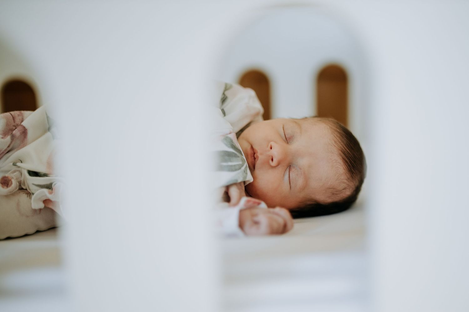 Four intimate black and white photos show a sleeping baby swaddled in soft bedding at home.