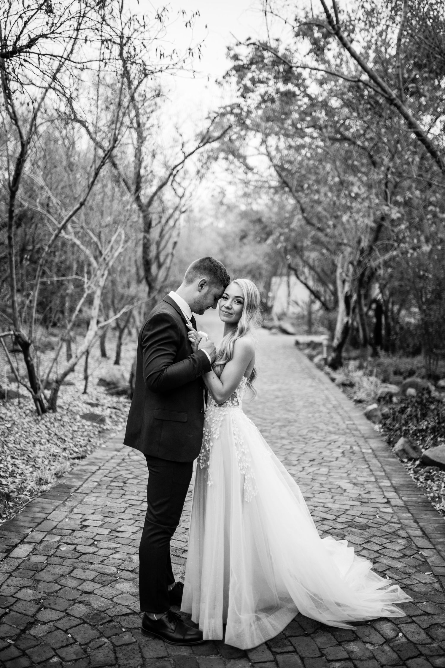 Romantic black and white photo sequence showing a couple dancing together on a cobblestone path surrounded by trees.