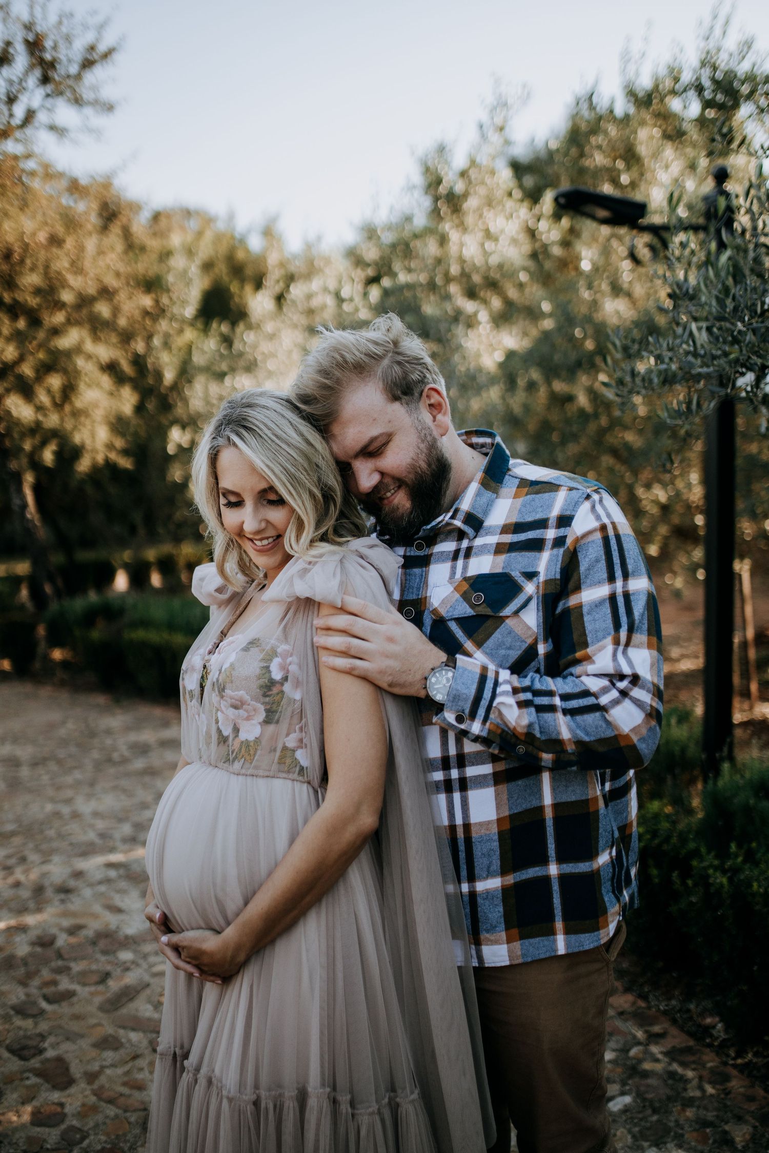 An intimate outdoor maternity photo session in a wooded area shows a couple embracing in soft autumn lighting.
