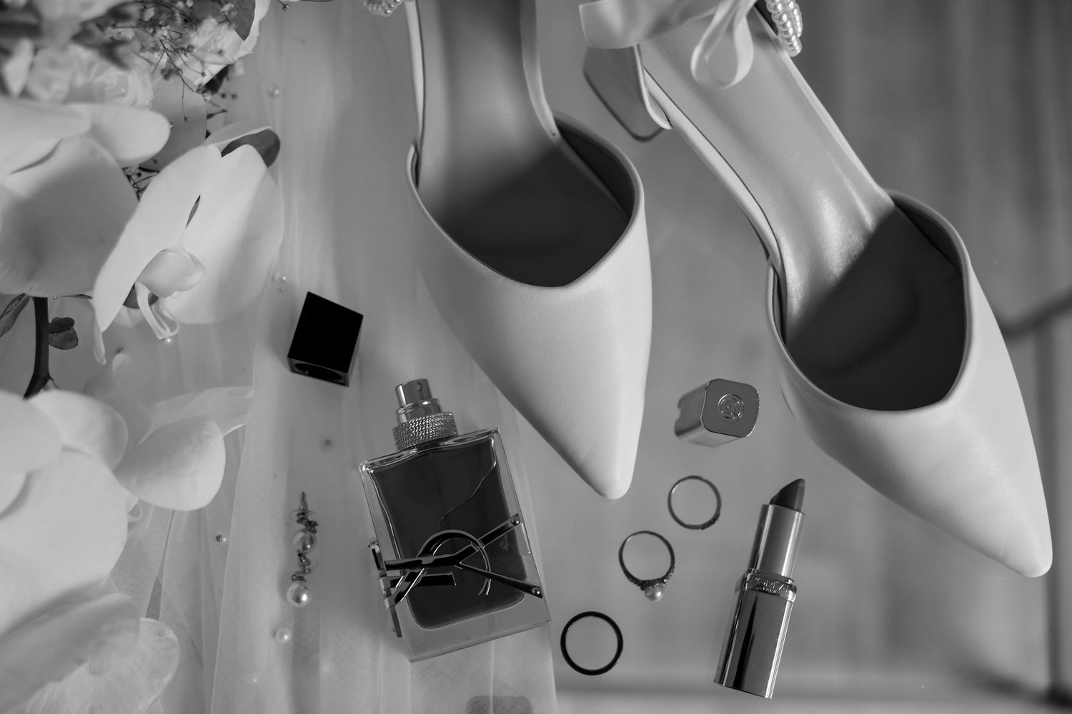 Black and white bridal accessories including white stiletto heels, perfume bottles and nail polish arranged artistically.