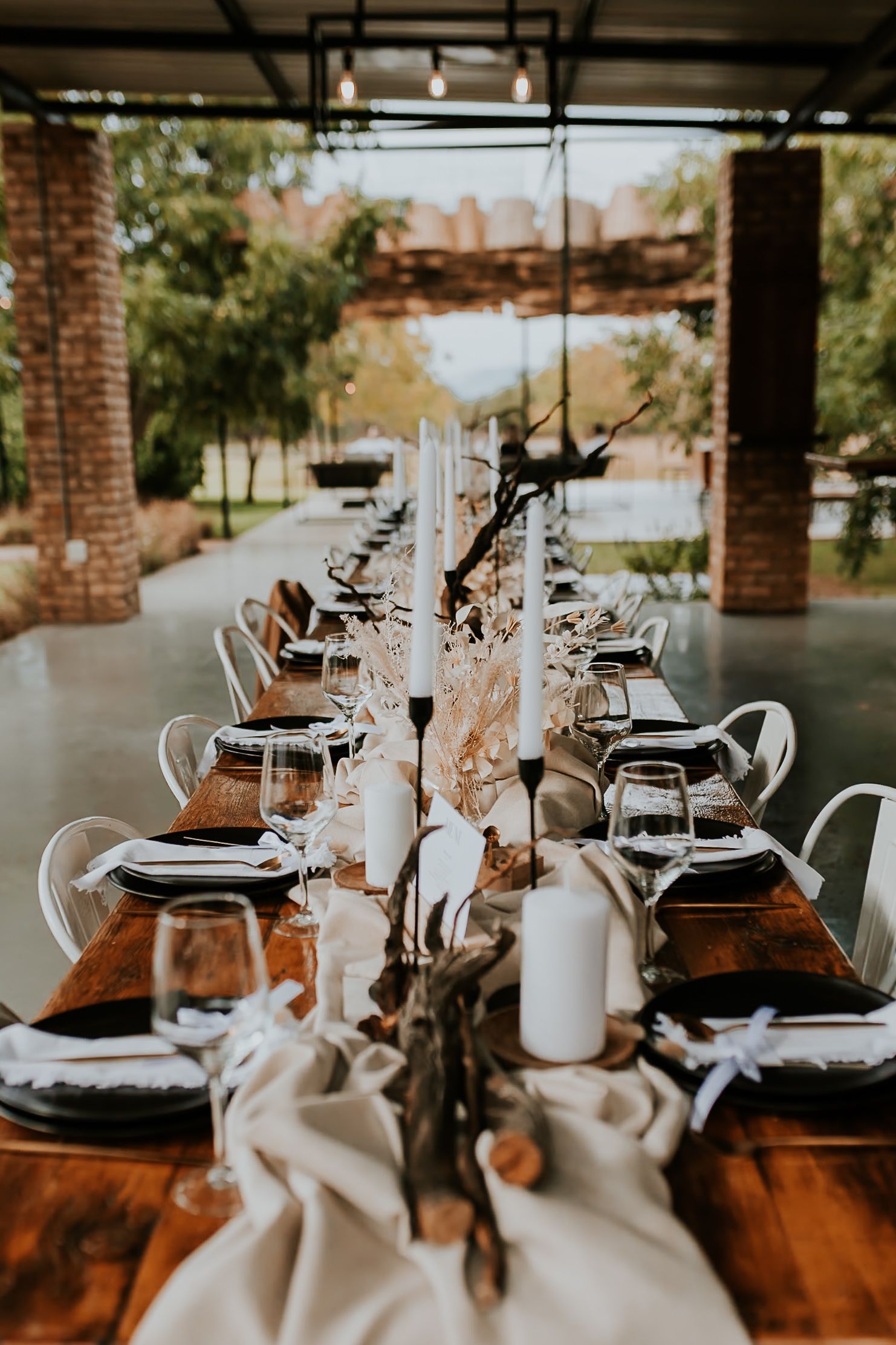Rustic wedding reception table settings with black plates and white ceramics on a wooden farmhouse table.