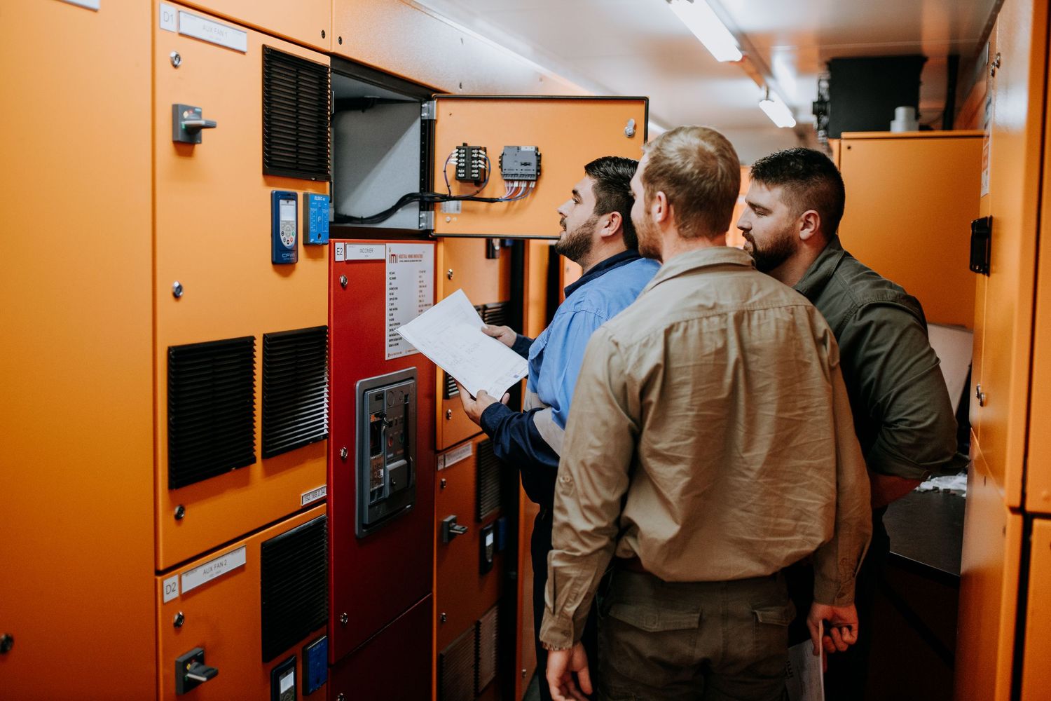 A row of orange-painted industrial electrical panels and control boxes line a wall in a service area.
