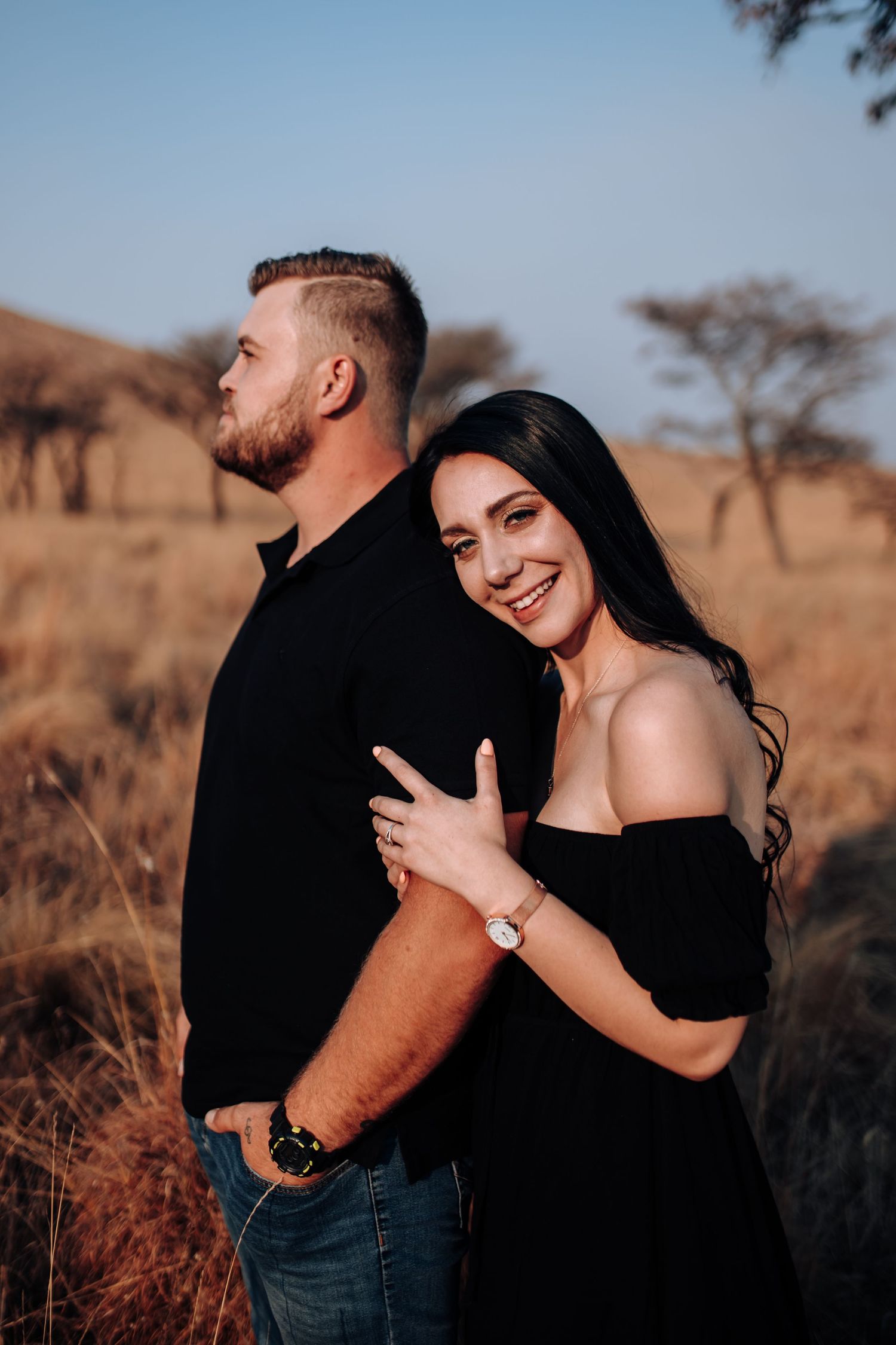 Romantic couple embraces and laughs together in warm evening light against a desert landscape with acacia trees.