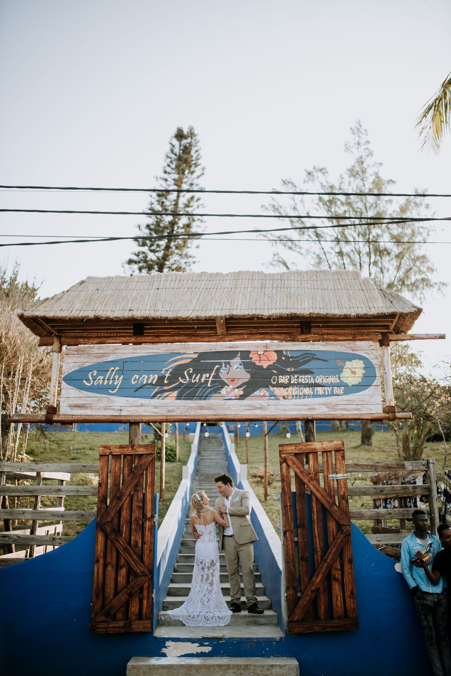 Rustic wedding ceremony entrance at Sally and Surf venue with wooden gates and blue signage under power lines.