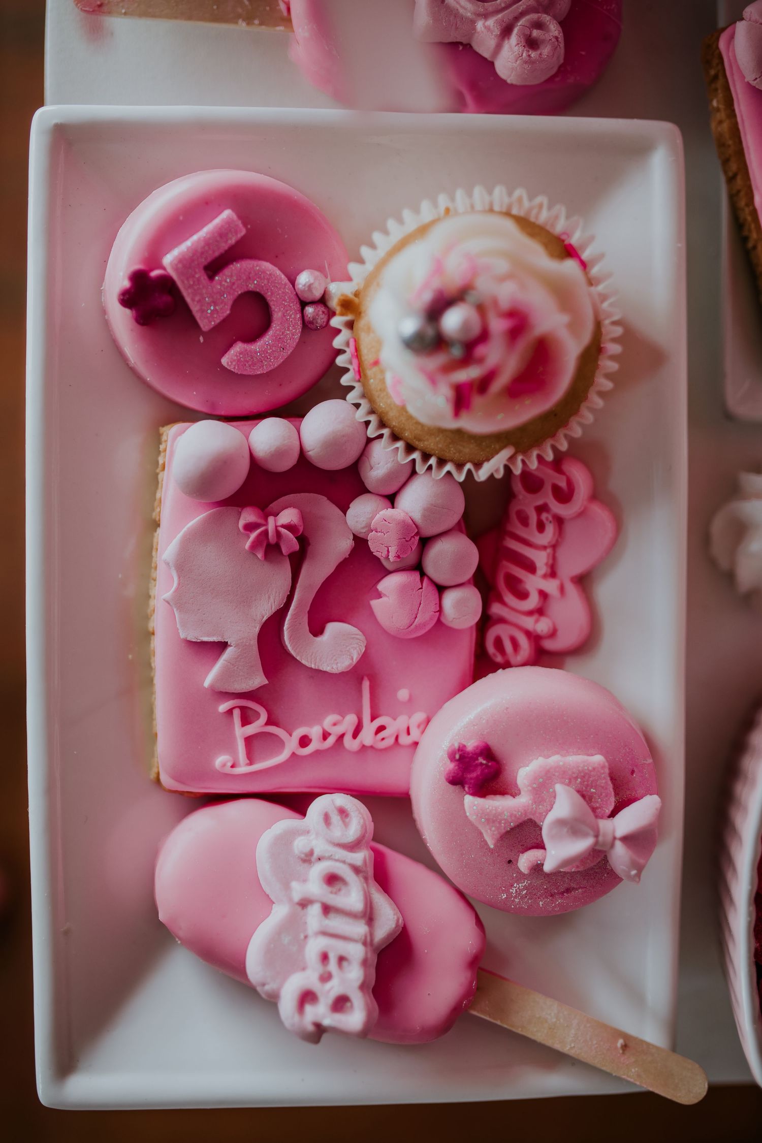 Pink fondant decorations with flowers and bows arranged on white porcelain plates create delicate pastry garnishes.