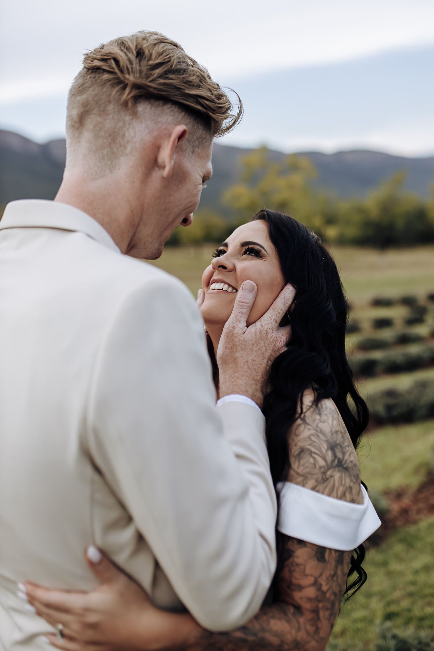 A romantic couple embraces in a scenic outdoor mountain setting during a photo session.