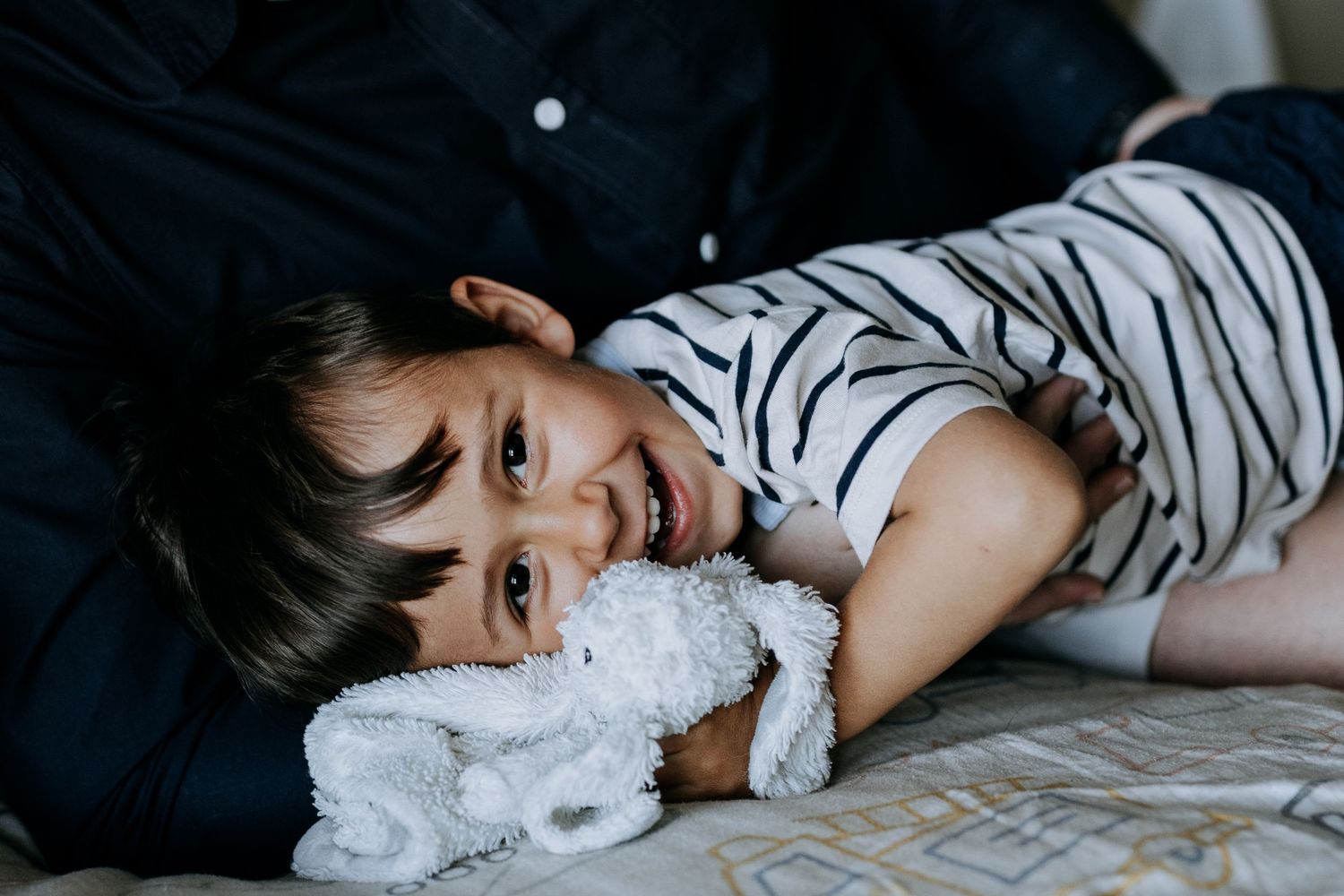 A series of black and white lifestyle photos showing a child lying down with a small white stuffed animal.