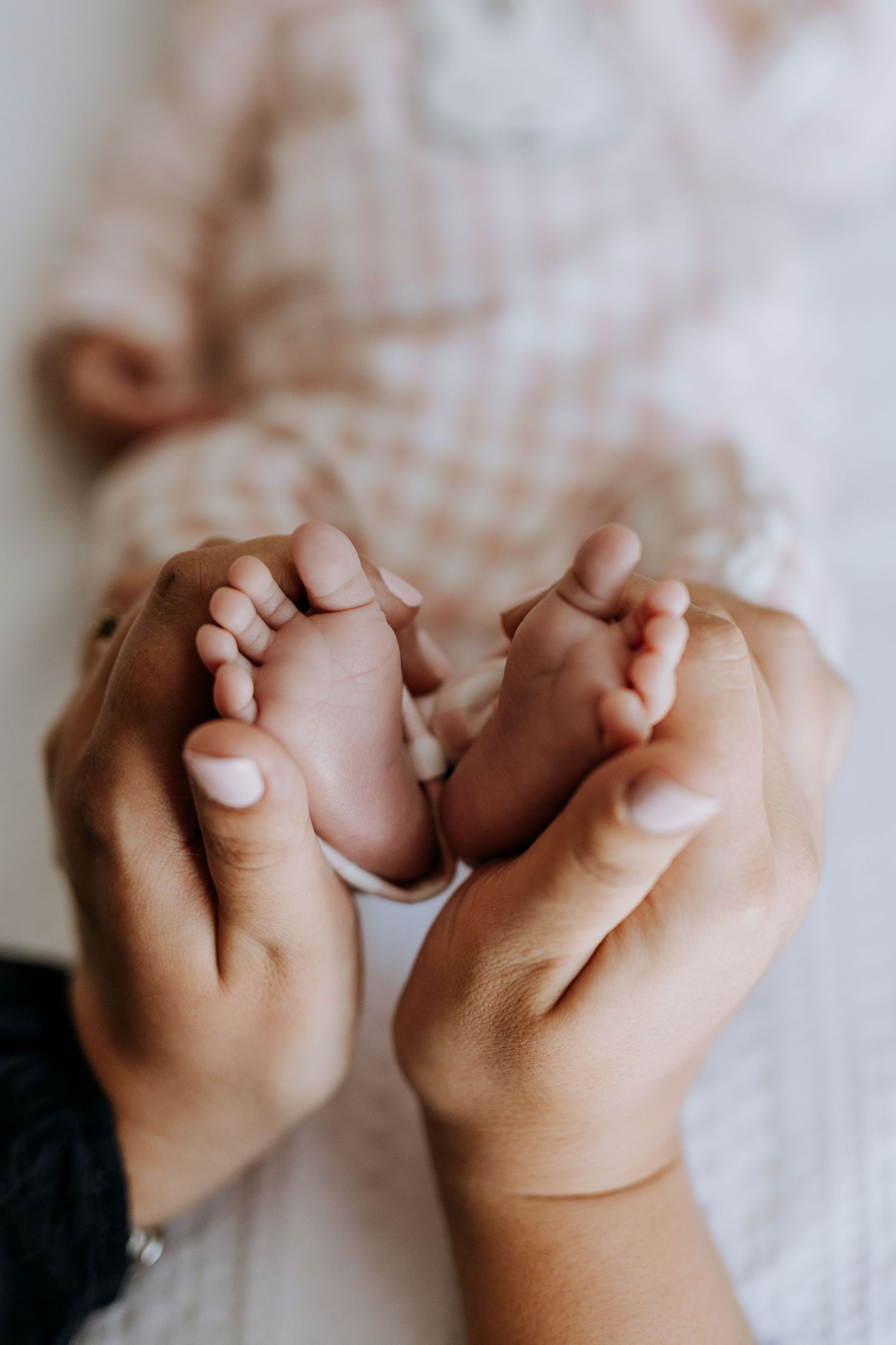 Adult hands gently cradling tiny newborn baby feet, showcasing the delicate bond between parent and child.