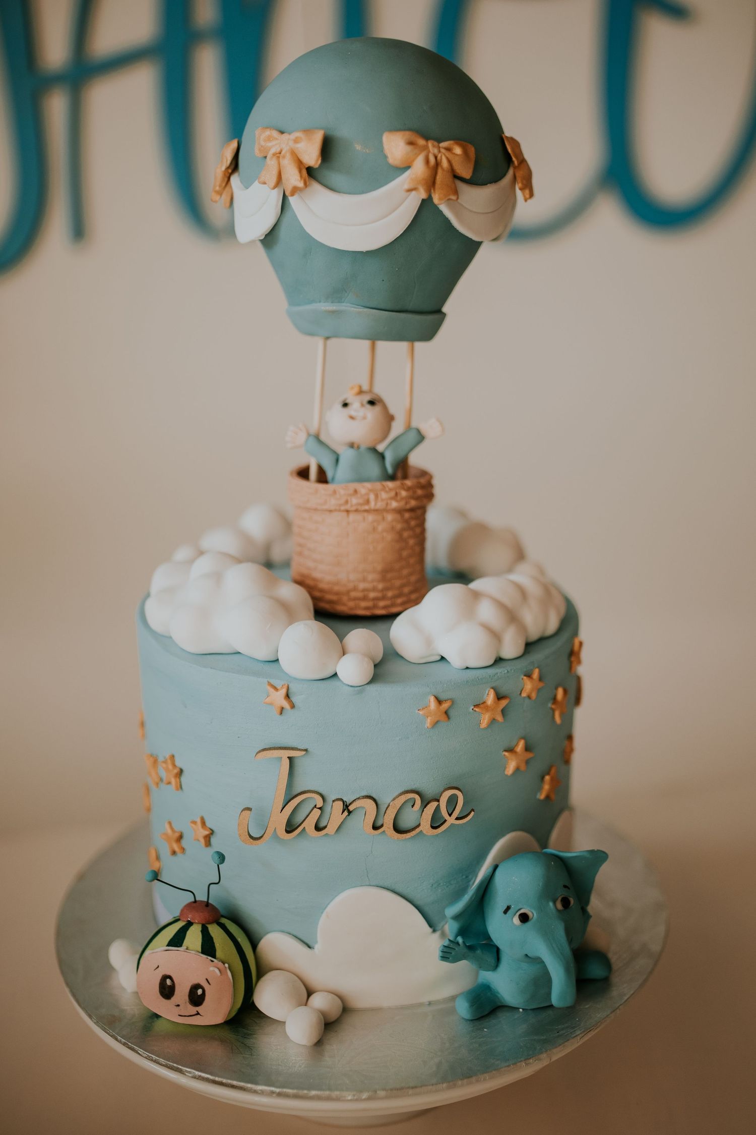 Baby shower cake with hot air balloon, elephant figure and clouds decorated in soft blue and gold tones.