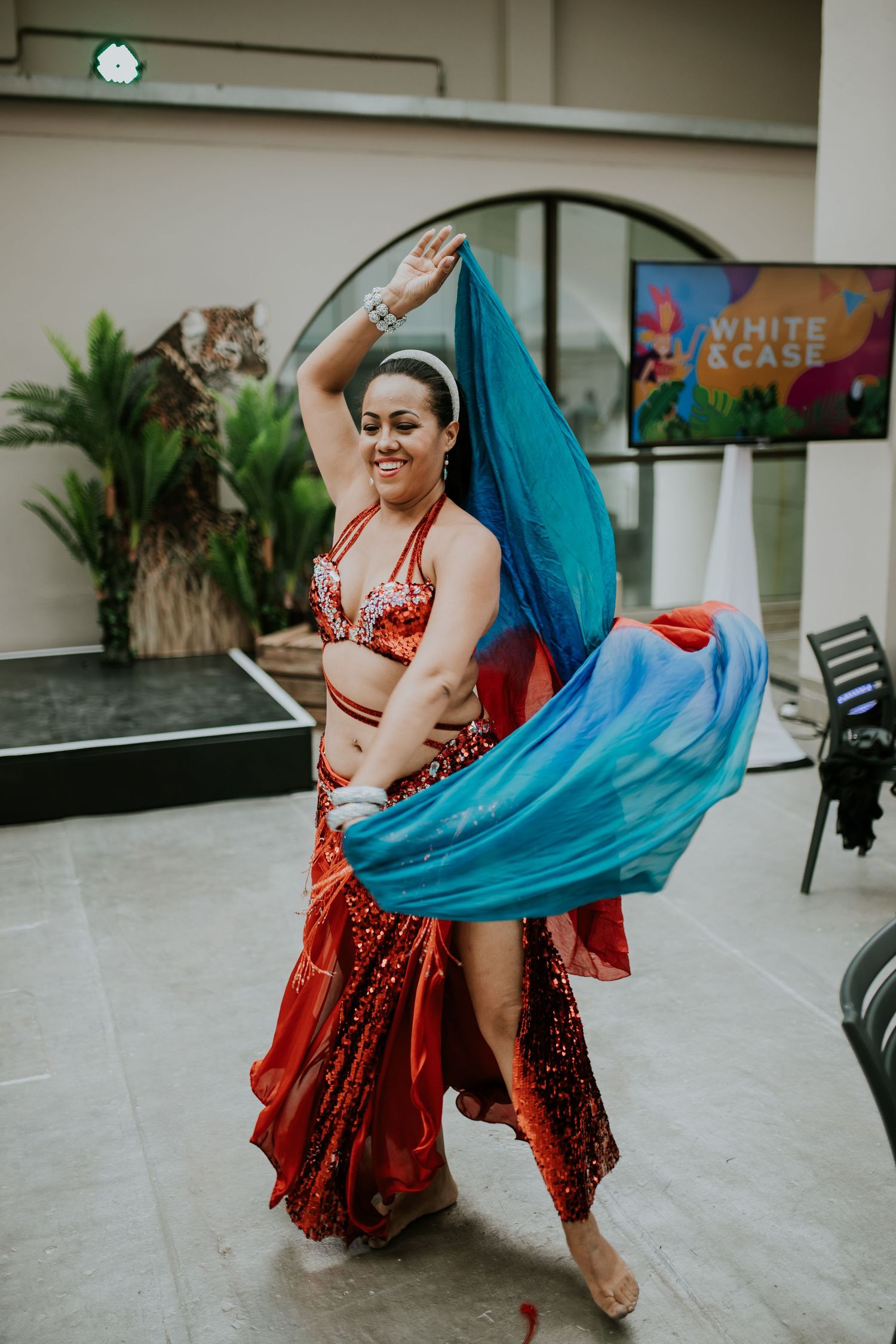 A dancer in a red sequined costume twirls with a flowing turquoise veil in a graceful performance series.
