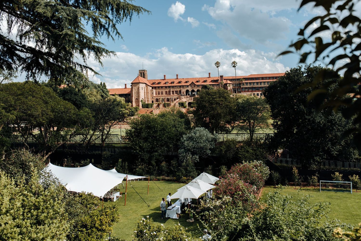 Scenic panoramic view of a historic red-brick building complex nestled among green hills under a blue summer sky.