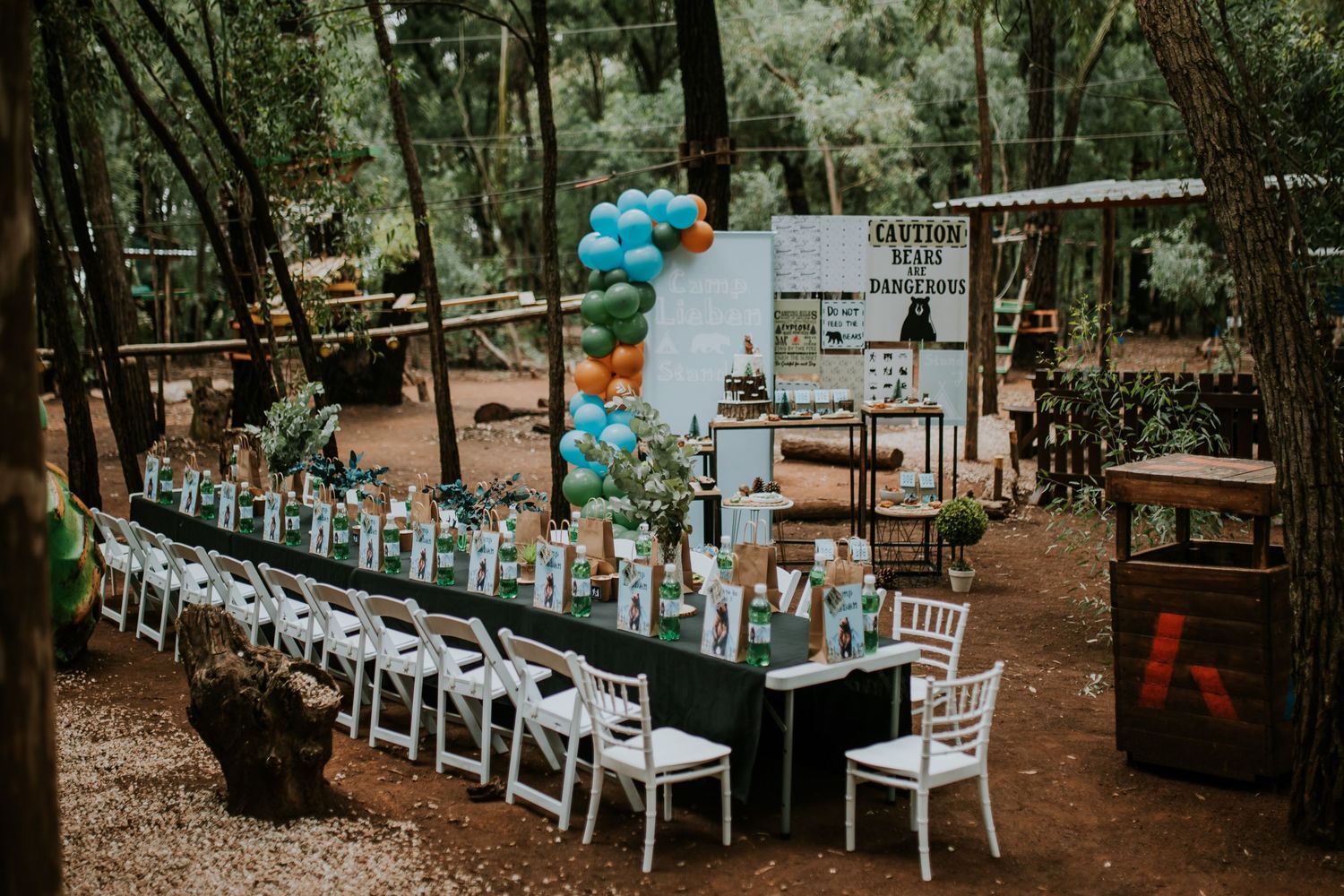 Forest wedding reception setup with white tables, teal accents and string lights creating an enchanted atmosphere.