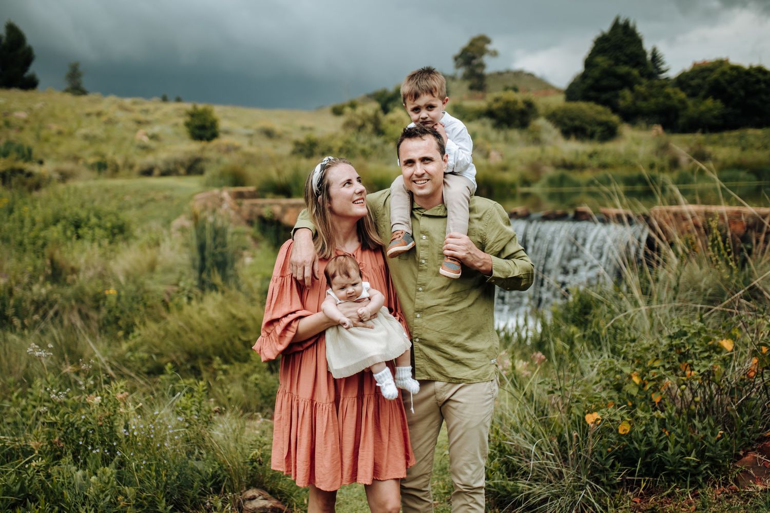 Couple in a rustic outdoor setting with dramatic storm clouds overhead and rolling hills in the background.