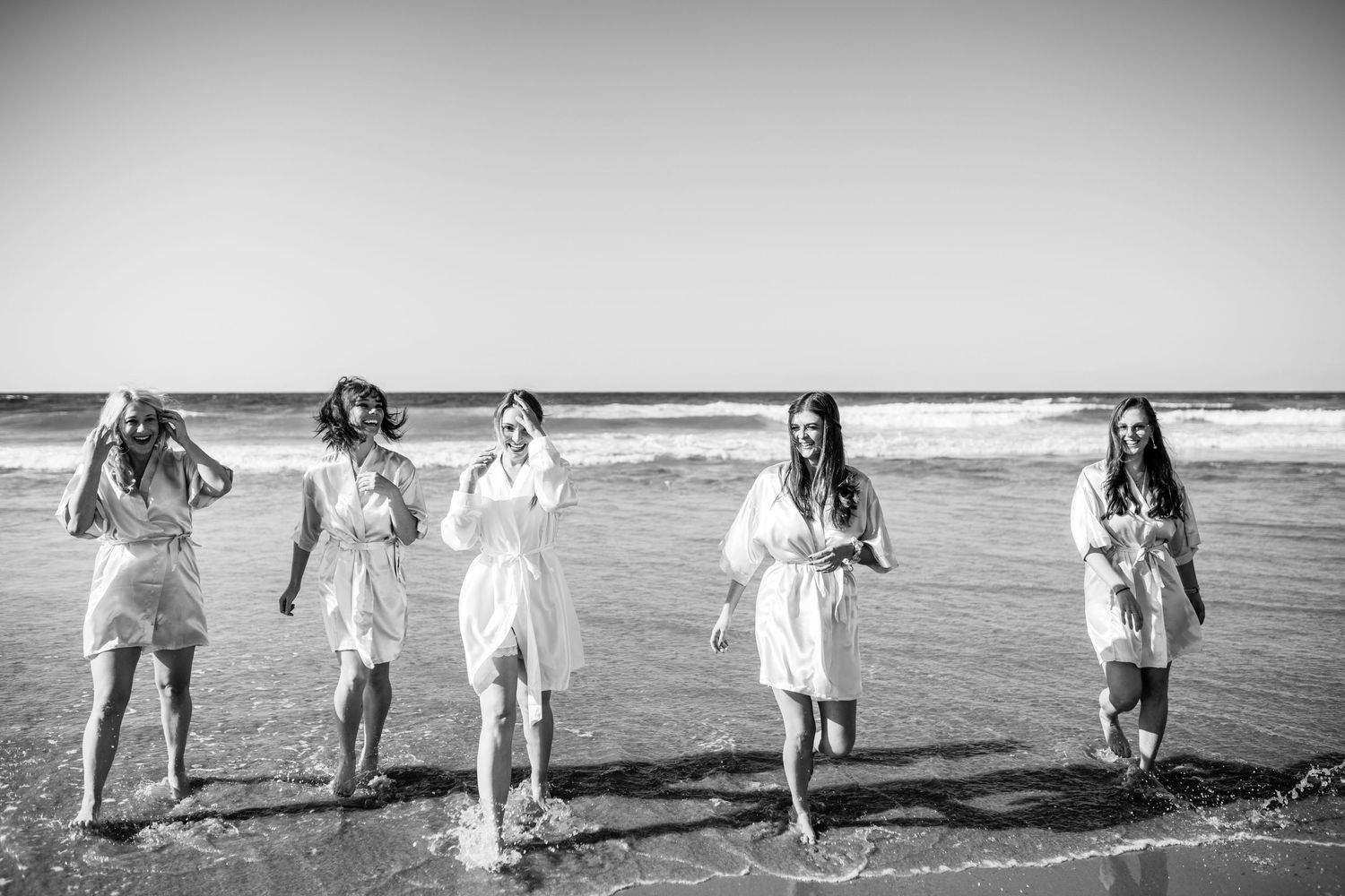 A group walks along a scenic beach shoreline together, their silhouettes framed against the ocean waves.