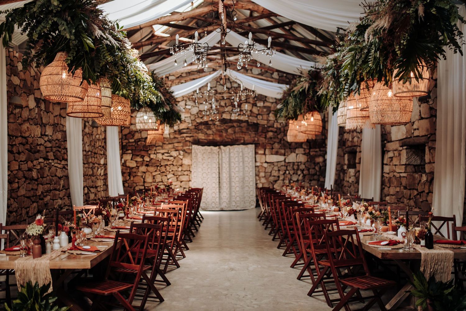 Elegant wedding reception venue with exposed brick walls, rocking chairs and hanging string lights creates rustic ambiance.