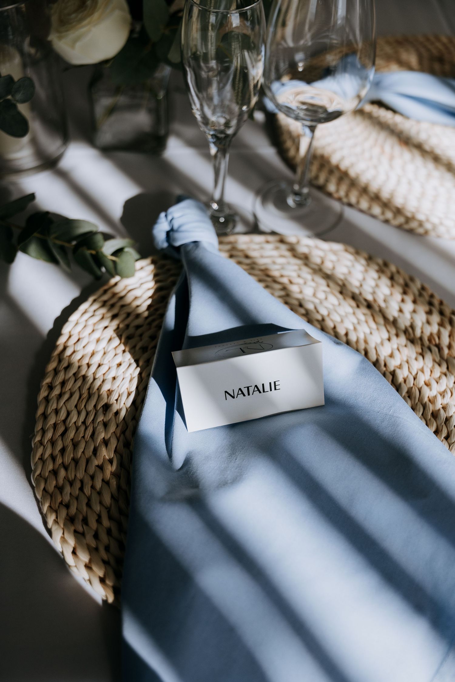 Place setting at an elegant event featuring woven placemats, wine glasses and nametags cast in dramatic shadows.