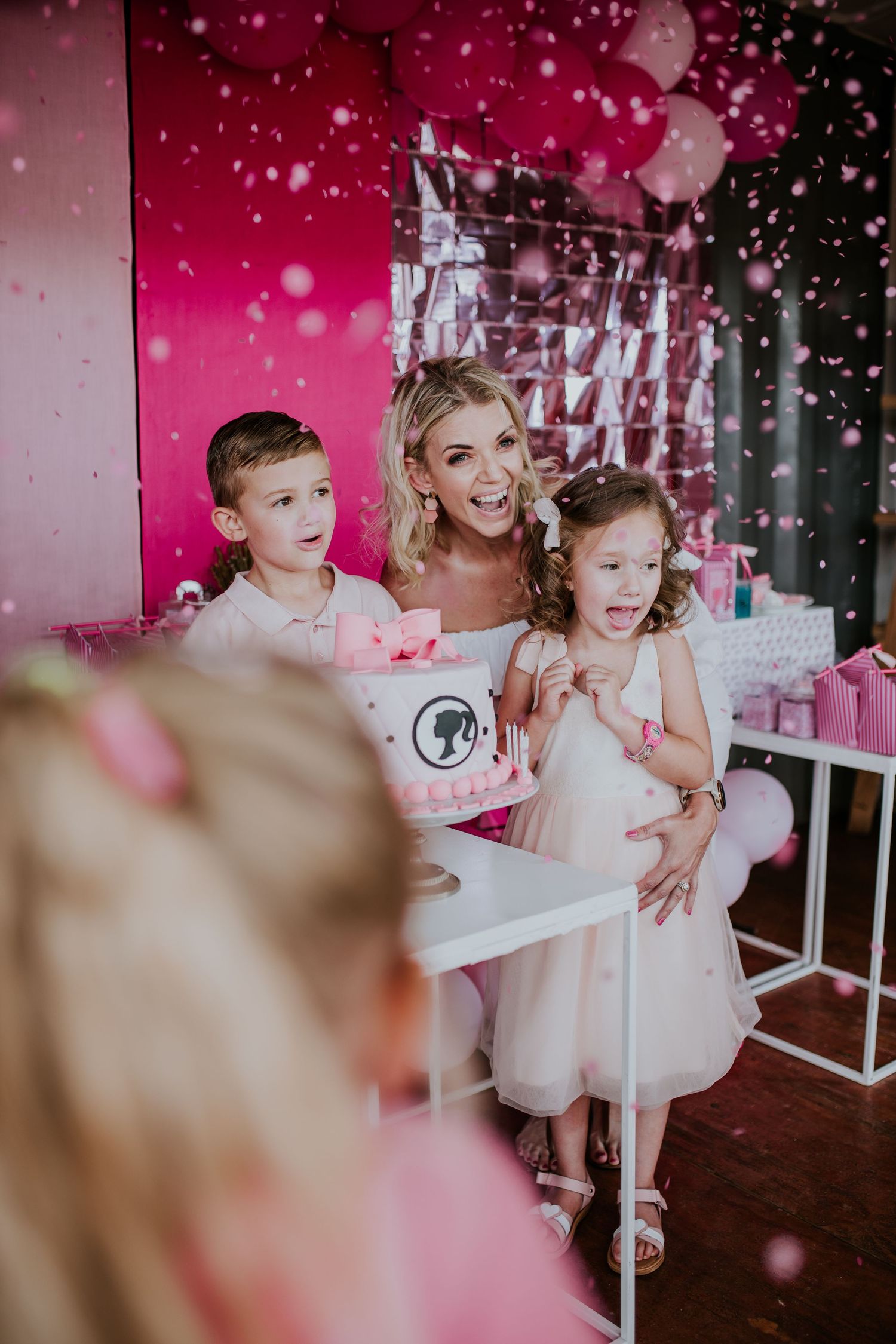 Mother and child playing in pink winter wonderland with falling sparkly snowflakes during holiday photoshoot.