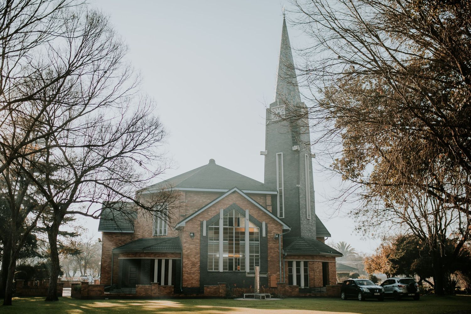 Traditional brick church building with tall white steeple and large windows captured during autumn season.
