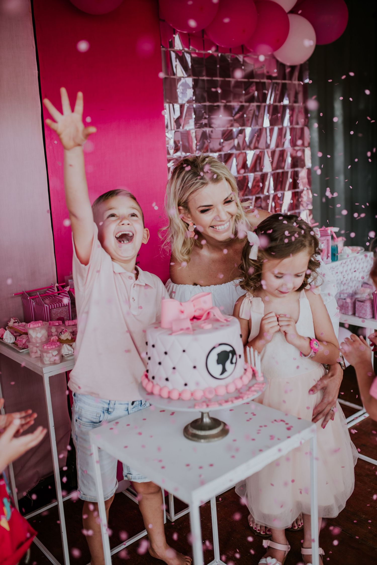 Joyful birthday celebration with children in tutus gathering around a pink cake while glitter falls in a pink-themed room.