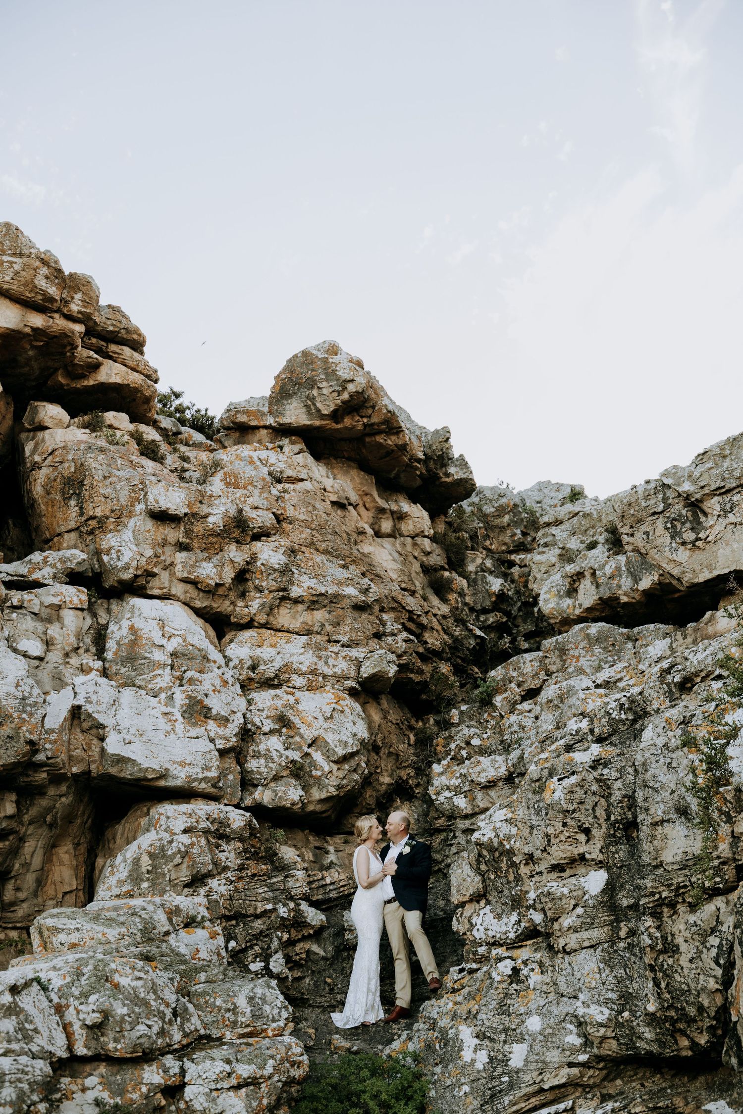 A couple in wedding attire embrace against dramatic rocky cliffs in a series of black and white photographs.