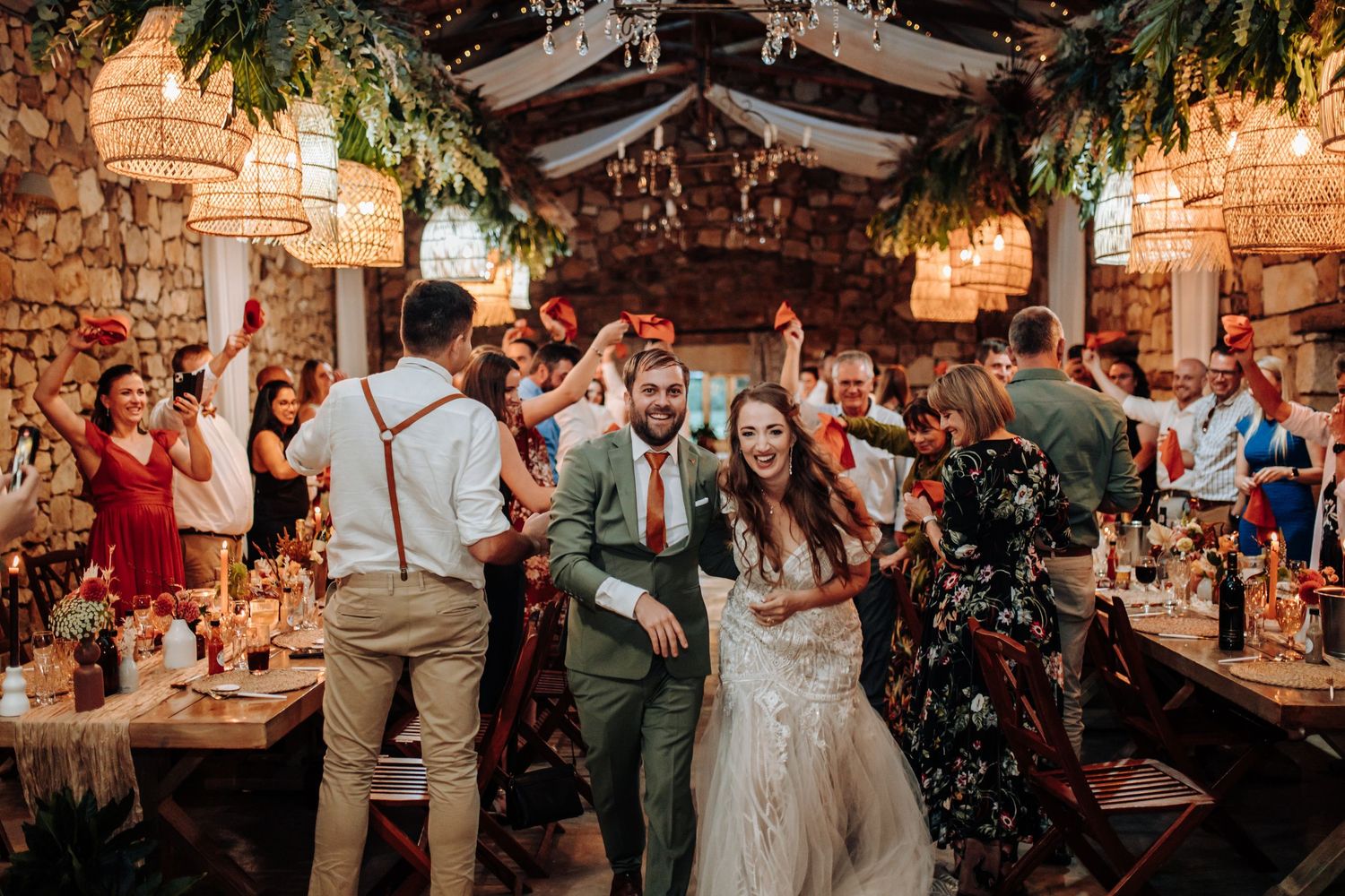 Newlyweds celebrate with guests during a rustic indoor wedding reception with string lights and stone walls.