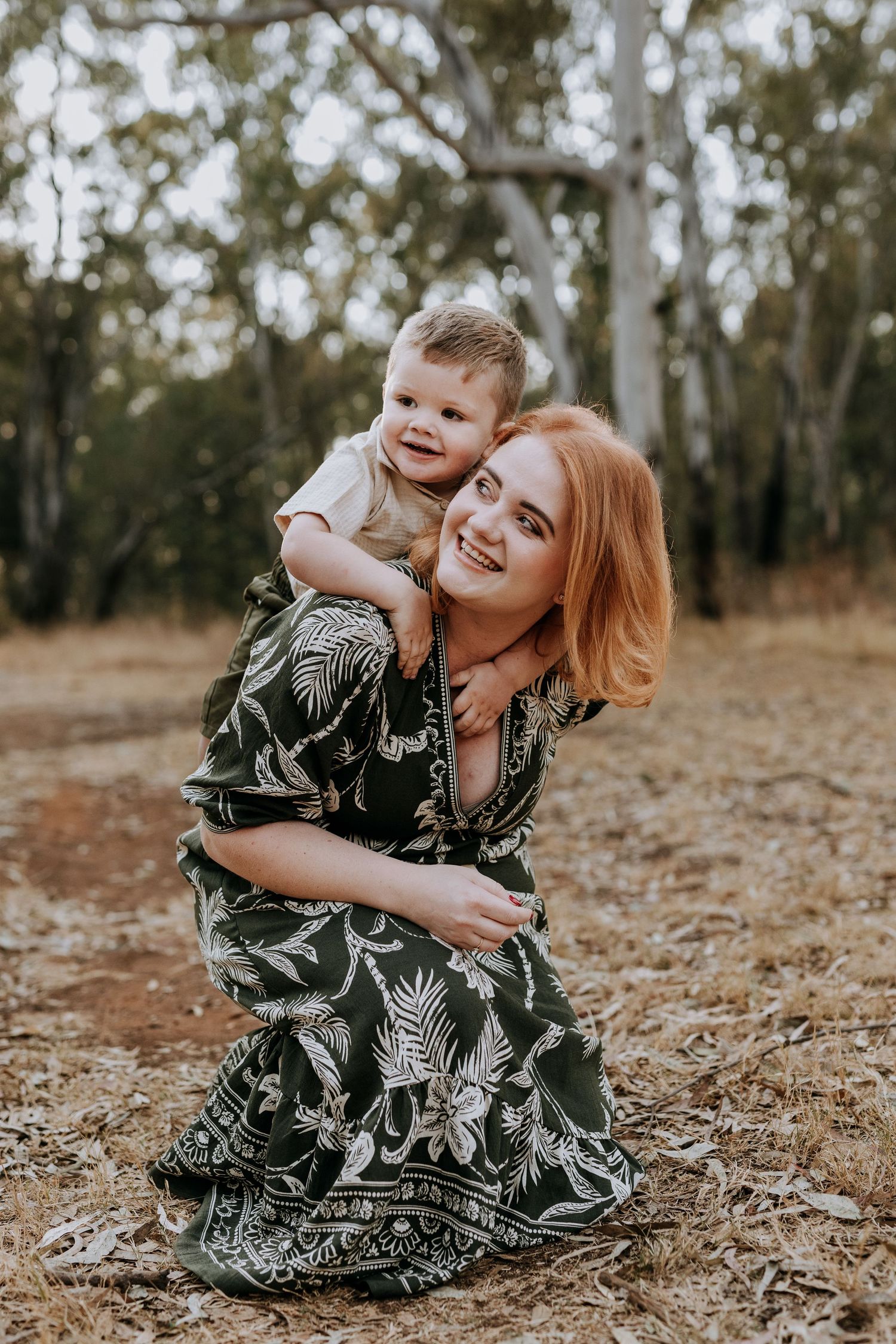 A tender moment captured outdoors as two people share joyful embraces while sitting on autumn ground.