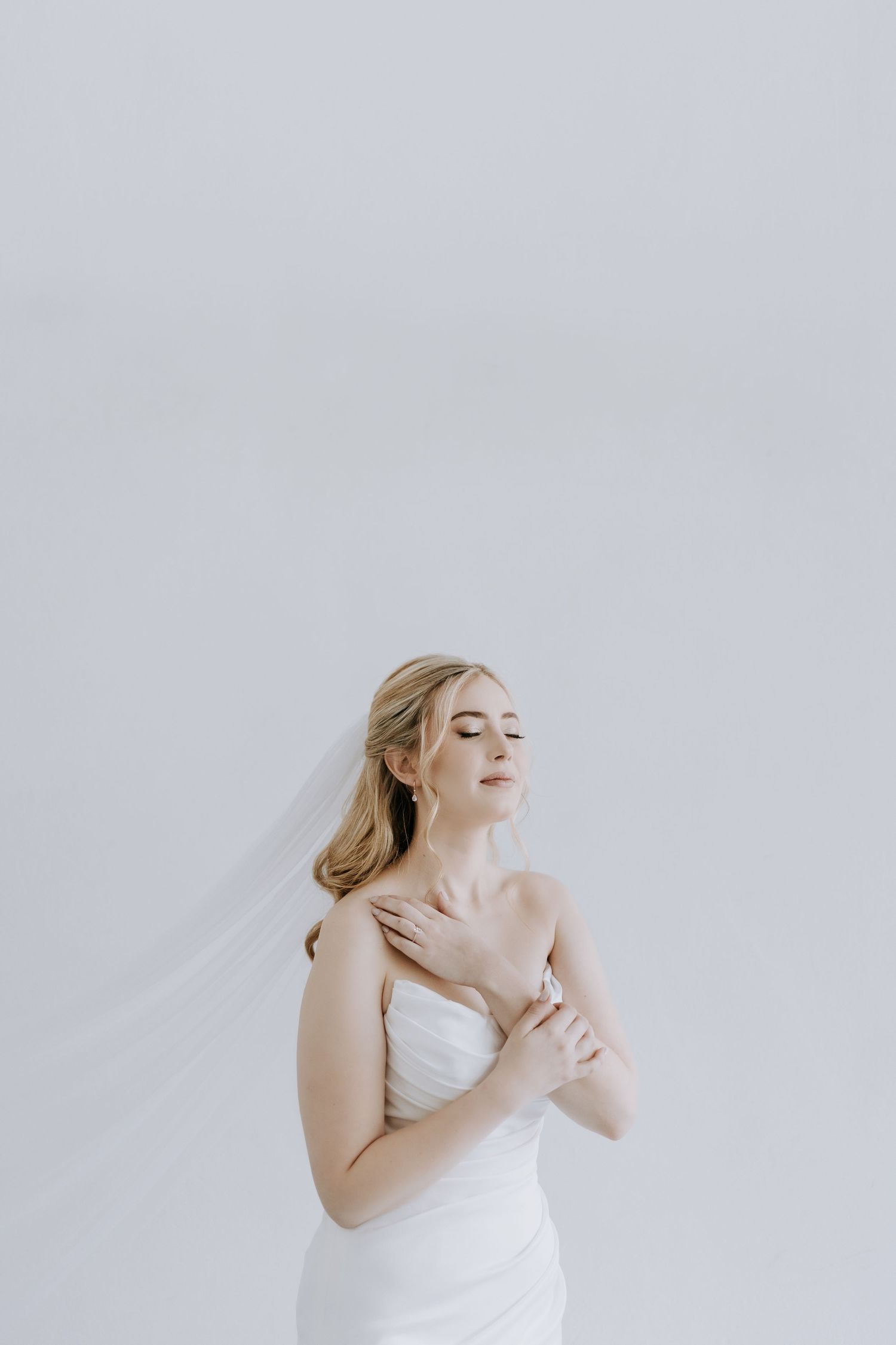 A bride in a white strapless wedding dress poses elegantly against a light gray backdrop.