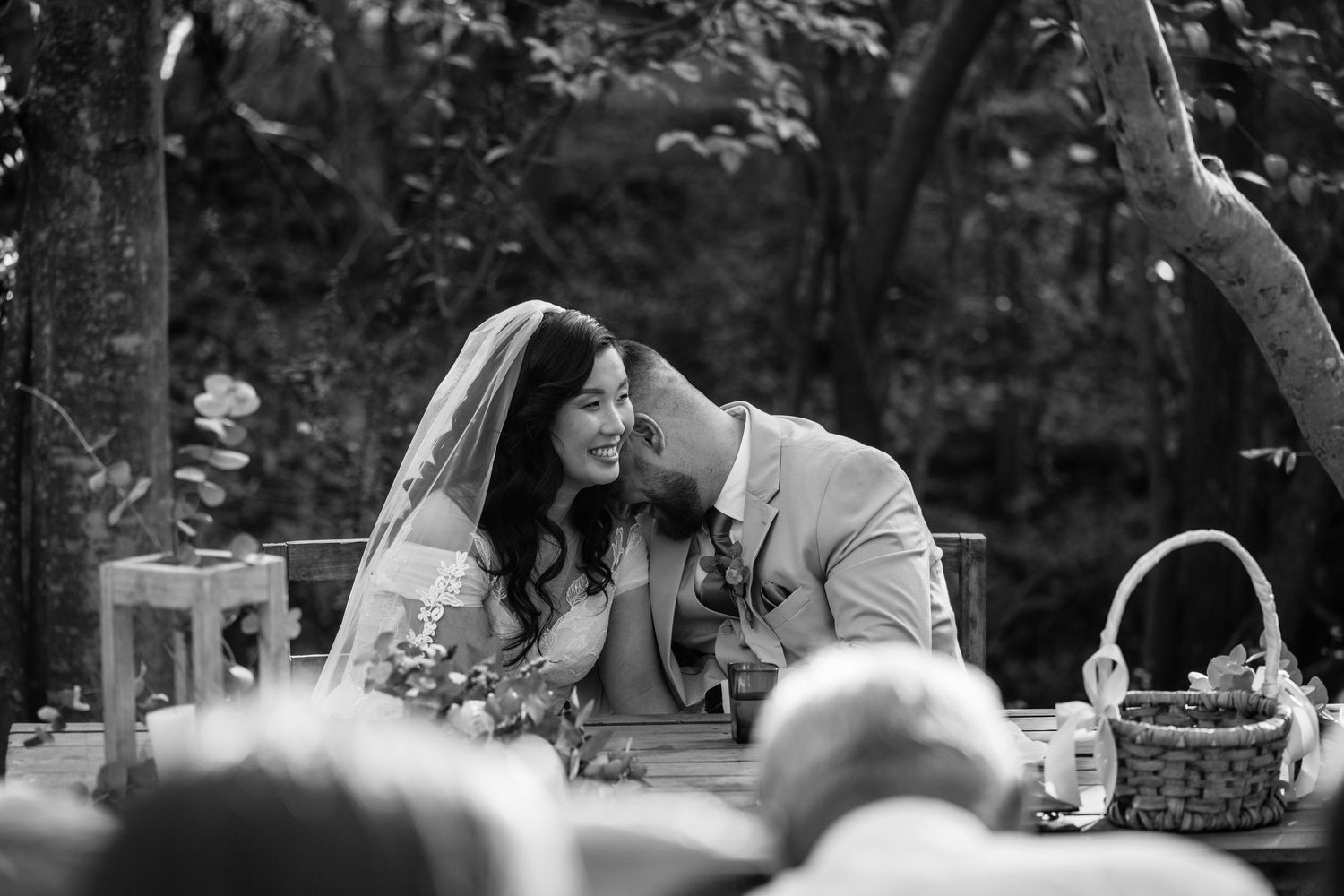 Two people kiss and embrace during an intimate black and white outdoor wedding photo session in nature.